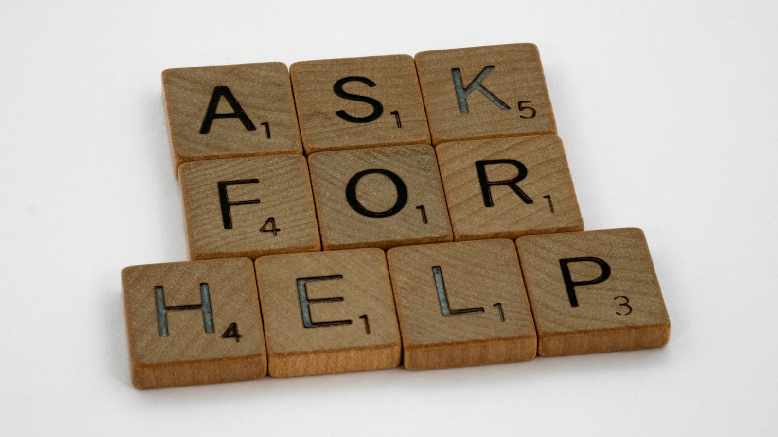 Wooden letter tiles spelling out 'ask for help' on a white surface