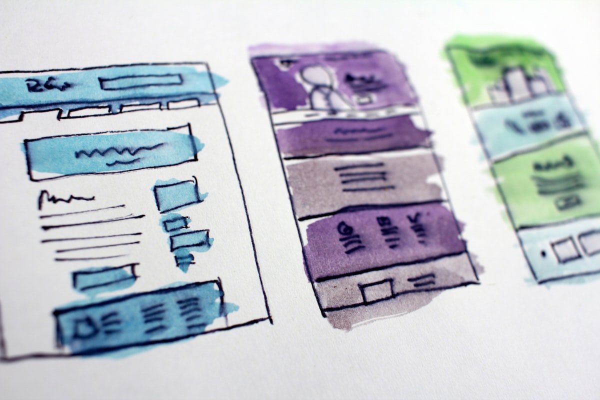 Hand-drawn watercolor wireframe sketches of three website page layouts on paper